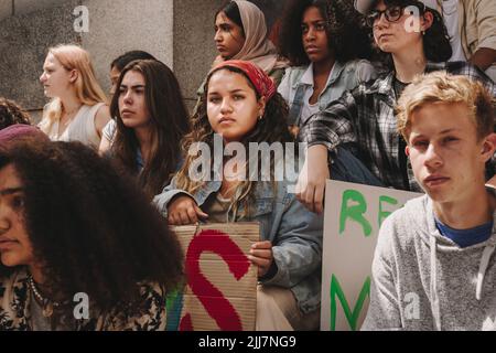 Youth climate activists sitting outside a building with placards and banners. Group of multicultural demonstrators protesting against global warming a Stock Photo