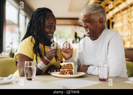 Senior couple smiling at each other while sharing a delicious cake in a cafe. Happy senior couple having a good time in a restaurant. Cheerful mature Stock Photo