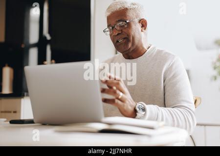 Mature businessman speaking during a virtual meeting in his home office. Senior businessman having a video conference with his colleagues while workin Stock Photo