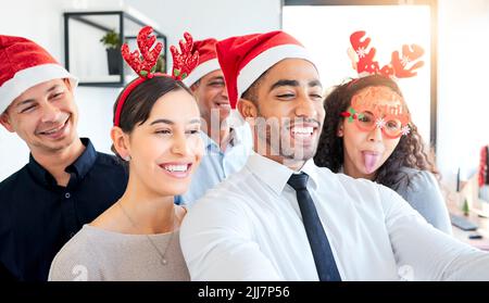 Some Christmas time fun. a group of businesspeople taking a selfie at work. Stock Photo