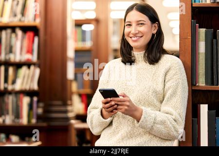 Making plans with friends. a young female student using a phone in a library at college. Stock Photo