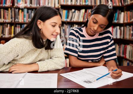 Whats the next question. two young female students studying together in a library at college. Stock Photo