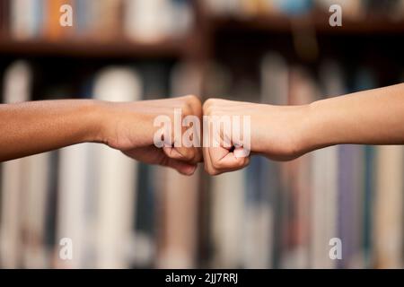 Were going to achieve great things. two unrecognizable people giving each other a fist bump in a library at college. Stock Photo