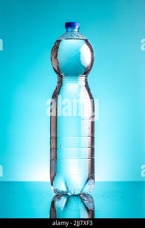 Plastic cold bottle of water with water drops on a blue background. Stock Photo