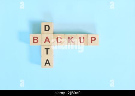 Data backup concept in computer and information technology. Wooden blocks crossword puzzle flat lay in blue background. Stock Photo