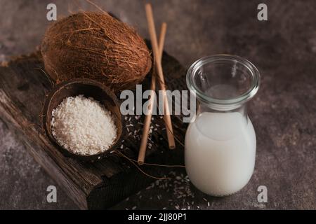 Bottle of coconut vegan milk with straws, whole coconut and flakes on a dark background Stock Photo