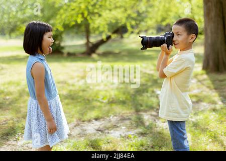 Cute little asian boy acting like a professional photographer while taking photos of his little sister Stock Photo