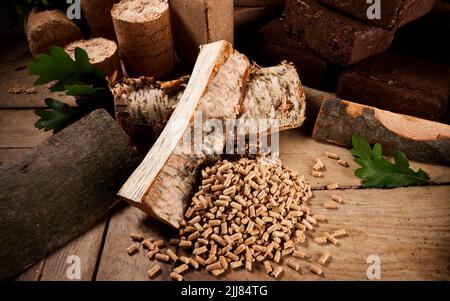 High angle of chopped birch and oak firewood scattered on wooden table near fuel pellets and cylindrical and square biomass briquettes Stock Photo