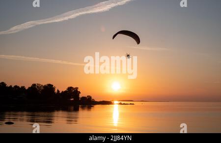 Paraglider pilot flies in the sky during sunset on beautiful beach. Paraplane silhouette. Adventure vacation and travel concept. Stock Photo
