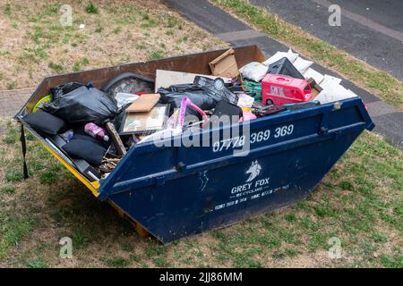 A skip full of household junk on a front lawn, UK Stock Photo