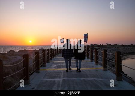 A couple walks hand in hand on a seaside pier during sunset. Stock Photo