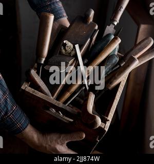 From above of crop male carpenter with wooden box full of various woodworking instruments Stock Photo
