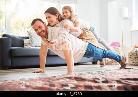 He lifts them up when theyre feeling down. a young father doing pushups with his wife and daughter on his back at home. Stock Photo