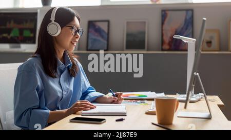 Asian Lady Working Online On Computer Taking Notes At Workplace Stock Photo