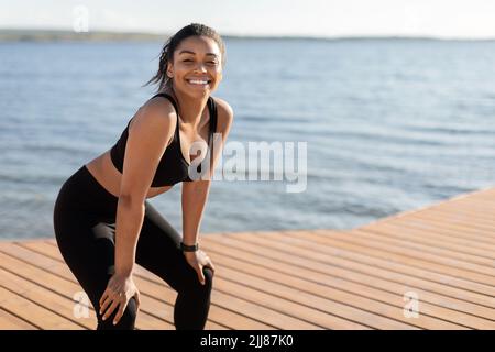 Cheerful african american lady training by seaside, having break Stock Photo