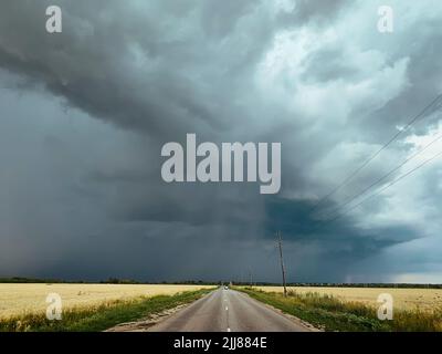 Storm clouds over asphalt road or route and fields. Stock Photo