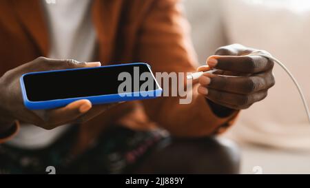 Black male hands plugging a charger in modern smartphone, using powerbank, closeup Stock Photo