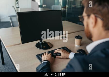 Unrecognizable businessman using computer with empty screen at office, sitting at workplace, offering space for mockup Stock Photo