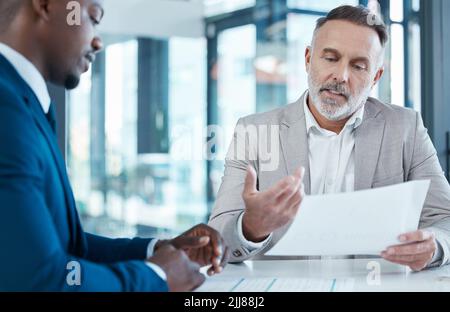 These numbers look good to me. two businessmen discussing paperwork in a modern office. Stock Photo