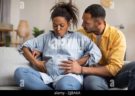 Pregnant African Woman Having Labor Pains, Husband Hugging Her Indoors Stock Photo