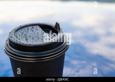 Takeaway paper coffee cups with plastic lids, sleeves on blue background with rail or water drops on the cap. Stock Photo