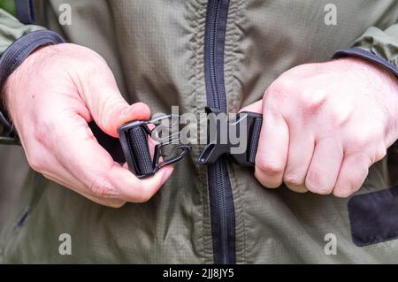 Fasten the waist belt of the backpack. Connect the latch with both hands. Connect the lock with your hands. Front view. Stock Photo