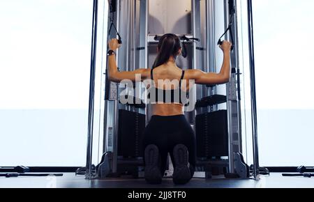 Sporty woman exercising on multistation at gym for arm and shoulders muscles. Fitness exercising in gym. Stock Photo