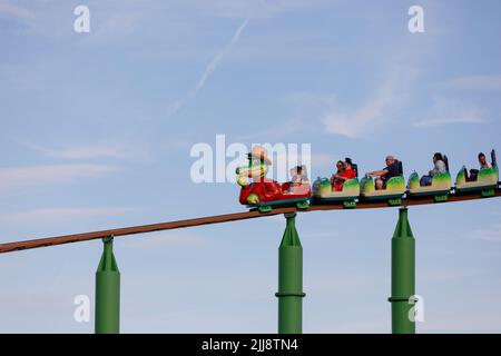 Children on a roller coaster with crocodile cartoon character lead car. Isolated against clear sky background. Green Scream, Adventure Island Stock Photo