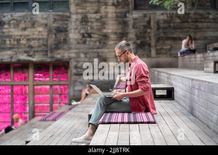 Thoughtful young 30s caucasian businessman in eyeglasses looking at laptop screen Stock Photo