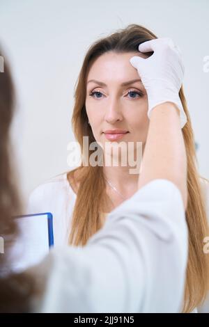 Hand in a glove, the doctor touches the forehead of the patient Stock Photo