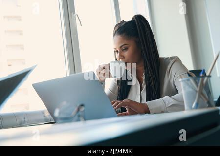Focused draftswoman using computer during coffee break Stock Photo