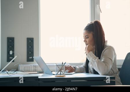 Concentrated young draftswoman working on portable computer Stock Photo