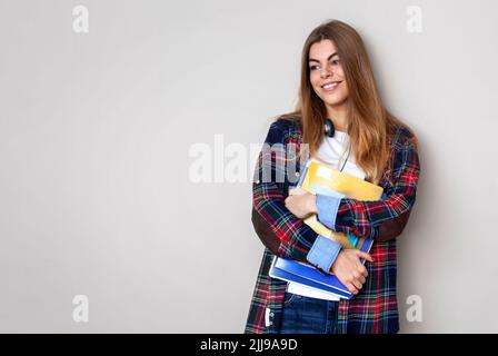 Studio portrait of young beautiful female student with books standing against wall. Stock Photo