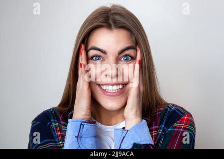 Studio portrait of happy surprised young woman in plaid shirt posing against wall. Stock Photo