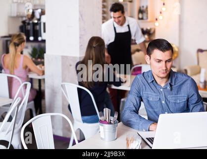 concentrated young man using laptop in modern cafe Stock Photo