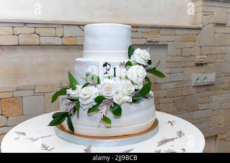 Beautiful big wedding cake with three storey decorated by tender sweet roses. White wedding cake with three levels and white roses Stock Photo