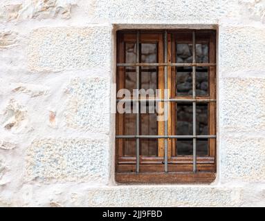 Old traditional rural home facade background with whitewashed wall and wooden brown window with protective safety bars. Property secure, rusty iron gr Stock Photo