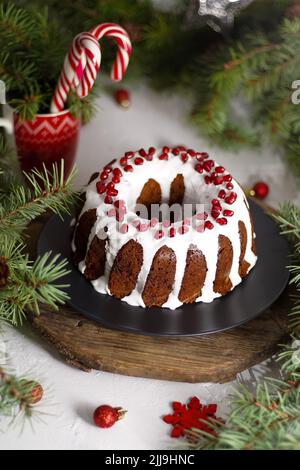 Christmas food. Round pie with white icing. Cupcake with a hole in the middle with pomegranate. Green spruce branches on the table. Still life. Sweet pastries, desserts and treats for the new year. Stock Photo