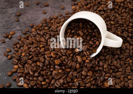 An overturned coffee cup with coffee beans spilled onto a metal surface with coffee beans spilled on it. Stock Photo