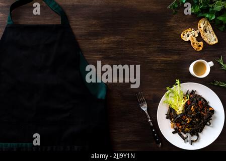 Dark wooden background with a culinary theme. The view is strictly from above. Apron and European dinner. Black cuttlefish ink pasta with seafood. Cof Stock Photo