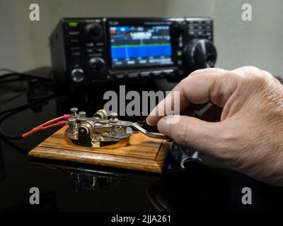 Selective focus of man's hand on a telegraph key with radio defocused in background Stock Photo