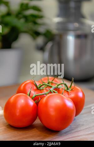Red tomatoes on vine in kitchen - sliced and whole fresh tomato on wood cutting board - ripe Solanum lycopersicum bunch and cluster Stock Photo