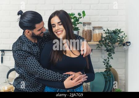 Long-haired caucasian woman tells her handsome bearded partner in patterned black shirt that she is pregnant. Happy news. Kitchen interior. High quality photo Stock Photo