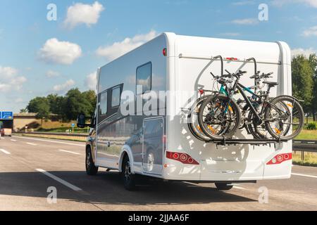 Scenic view big modern white family rv camper van vehicle driving on european highway road against blue sky in summer day. Rving motorhome lifestyle Stock Photo