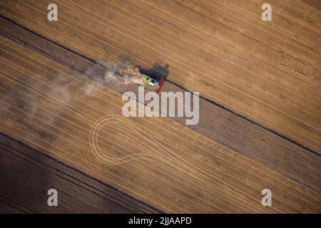 Agricultural machines harvest wheat in the field. Aerial shot from above. There is a lot of dust around the harvester. Stock Photo