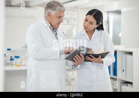 Working with her supervisor to solve the case. two scientists using a digital tablet together in a lab. Stock Photo