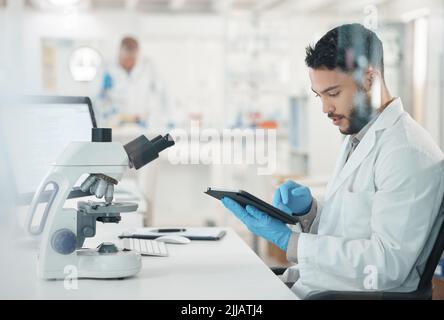 Making informed decisions based off his thorough research. a young scientist using a digital tablet while working in a lab. Stock Photo
