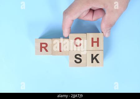 Risk to rich business concept. Hand changing words on wooden blocks in blue background. Stock Photo