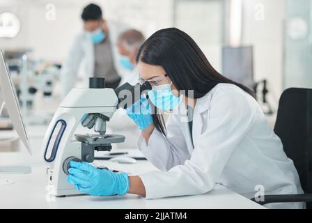 The best way forward is to keep at it. a young scientist using a microscope in a lab. Stock Photo