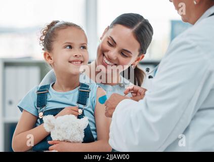 All done. a doctor putting a plaster on a little girls arm while administering an injection in a clinic. Stock Photo